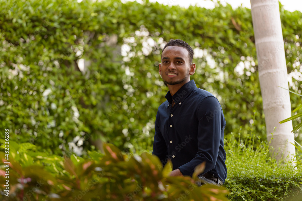 Young African businessman sitting outdoors at rooftop garden and smiling Young African businessman sitting outdoors at rooftop garden and smiling