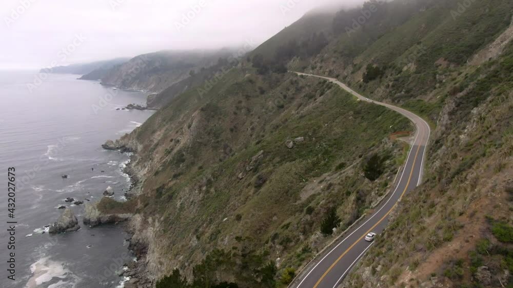 Aerial Shot Of Vehicles On Winding Coastal Road Over Mountain, Drone Flying Forward Over Coastline Against Sky - Big Sur, California Aerial Shot Of Vehicles On Winding Coastal Road Over Mountain, Drone Flying Forward Over Coastline Against Sky - Big Sur, California