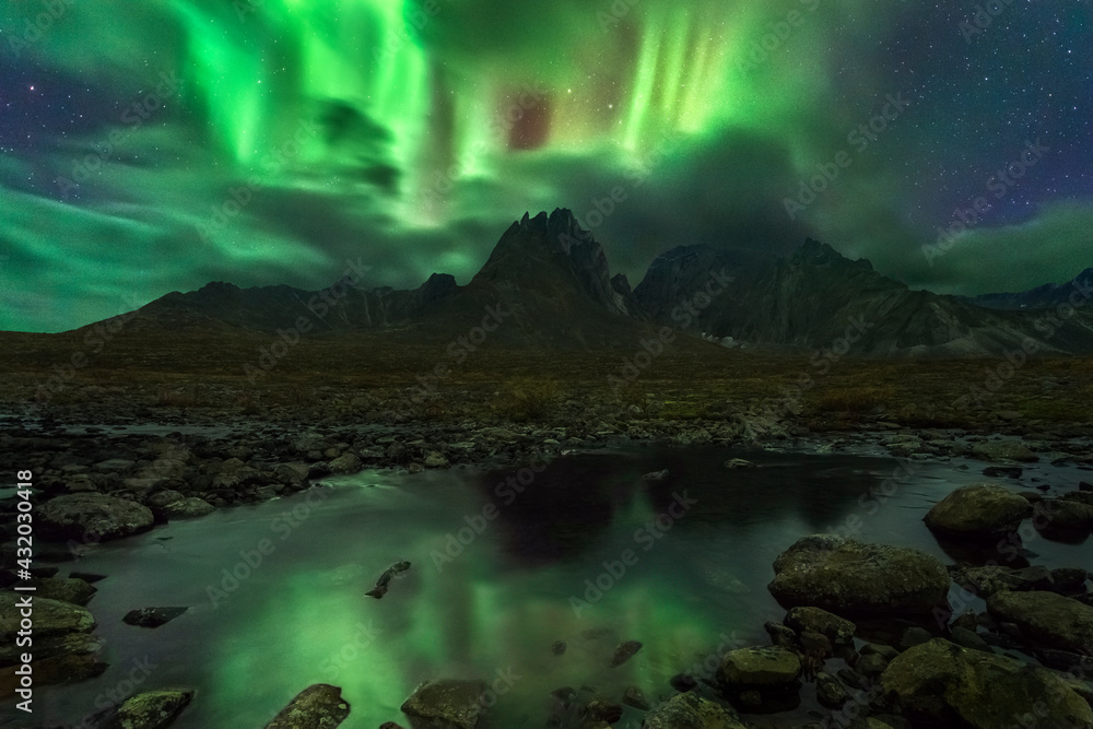 The aurora bursts through the clouds in the night sky reflected in a small tributary below, deep in the wilderness of the Ogilvie Mountains, Yukon Territory. The aurora bursts through the clouds in the night sky reflected in a small tributary below, deep in the wilderness of the Ogilvie Mountains, Yukon Territory.
