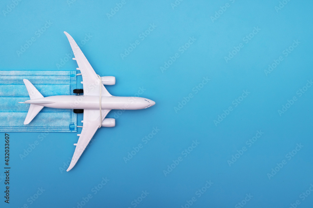 Naklejka premium A plane model with a medical mask on a blue background. Safety flight and travel during quarantine and lockdown. Safe travels concept. Opening borders