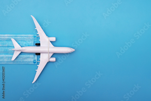 A plane model with a medical mask on a blue background. Safety flight and travel during quarantine and lockdown. Safe travels concept. Opening borders