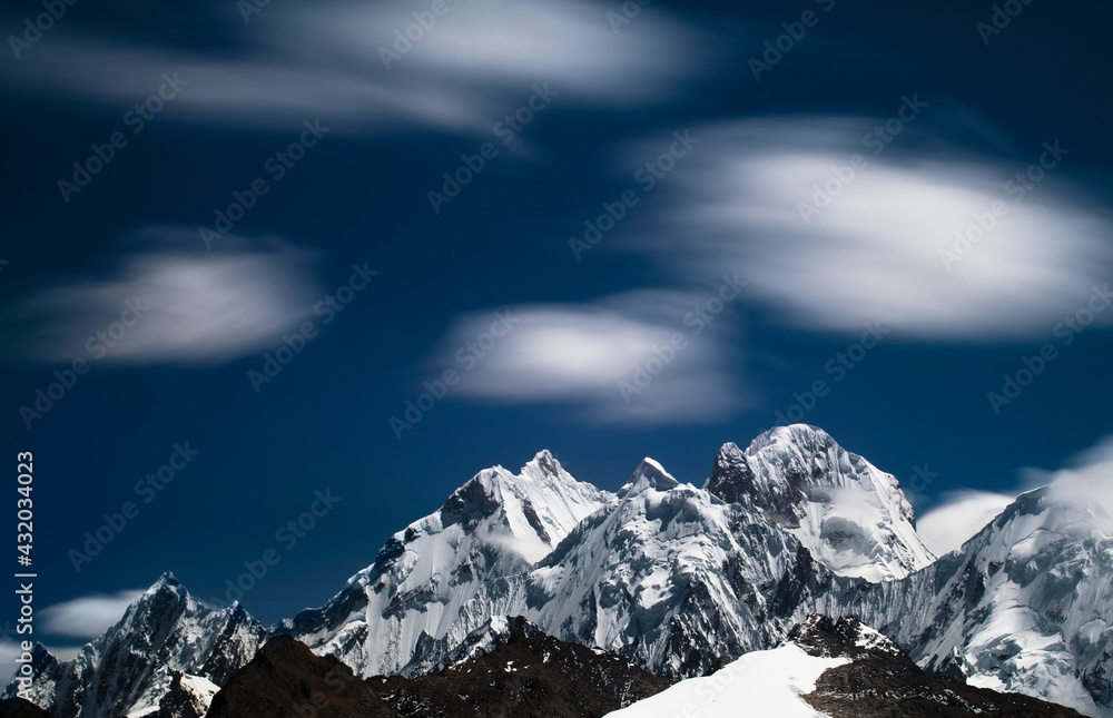 A telephoto view with motion blur of the clouds from Cuyoc Pass looking at the Peaks from tall right to left: Siulu Grande, Jurau, Sarapo in the Cordillera Huayhuash of the Andes Mountains in Peru.