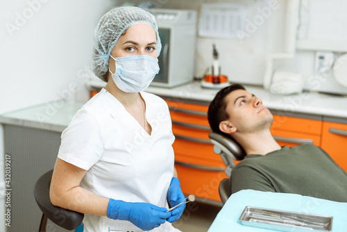Female dentist stands in the dental office. Happy patient on the background. Dental health and care concept