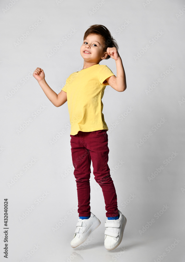 boy in a yellow T-shirt with free space and burgundy jeans is jumping on a light background. boy in a yellow T-shirt with free space and burgundy jeans is jumping on a light background.