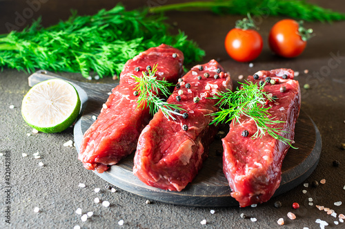 Raw beef steaks with herbs, spices and vegetables on dark kitchen table close up.