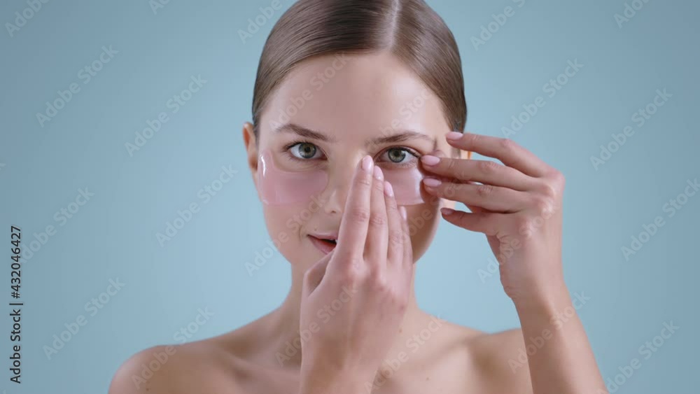 Portrait of pretty millennial woman putting eye patche and touching her face while looking to camera . Female model with naked shoulders and nude make up posing and smiling. Portrait of pretty millennial woman putting eye patche and touching her face while looking to camera . Female model with naked shoulders and nude make up posing and smiling.