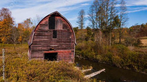 Abandoned Antique Red Barn with Rounded Roof Overhanging Creek Bank - New York © Sherman Cahal
