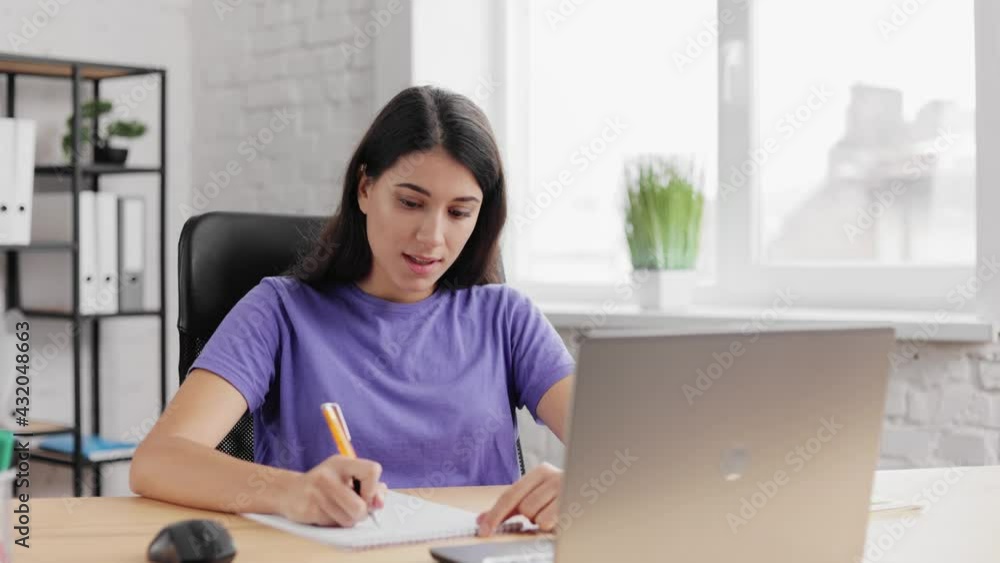Smiling young woman, conference calling on camera talks. Distance education. Brunette girl using laptop webcam, discussing business project and making notes. Female has conference calling in office. Smiling young woman, conference calling on camera talks. Distance education. Brunette girl using laptop webcam, discussing business project and making notes. Female has conference calling in office.
