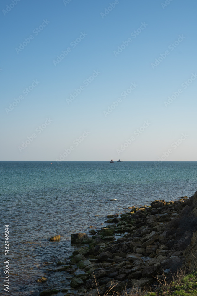 Rocky seashore, clear sky without clouds, two tugboats on the horizon. Rocky seashore, clear sky without clouds, two tugboats on the horizon.