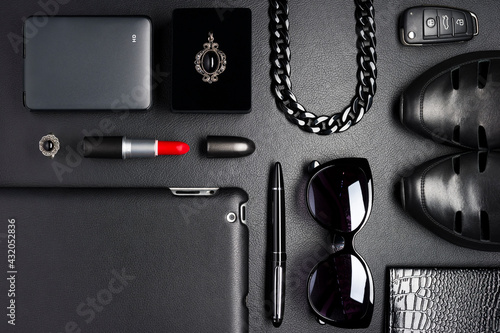 Woman accessories in business style, red lipstick, gadgets, shoes, jewelry, car key, sunglasses and other luxury businesswoman attributes on leather black background, fashion industry, top view