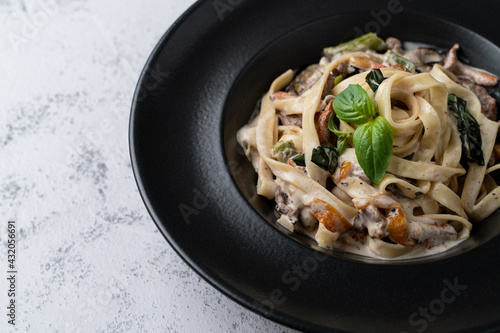 A black bowl of italian creamy and yummy pasta on a horizontal photo, a bowl is standing on the right