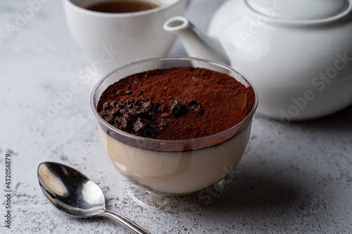 Classic tiramisu in a plastic glass with a spoon and tea set aside
