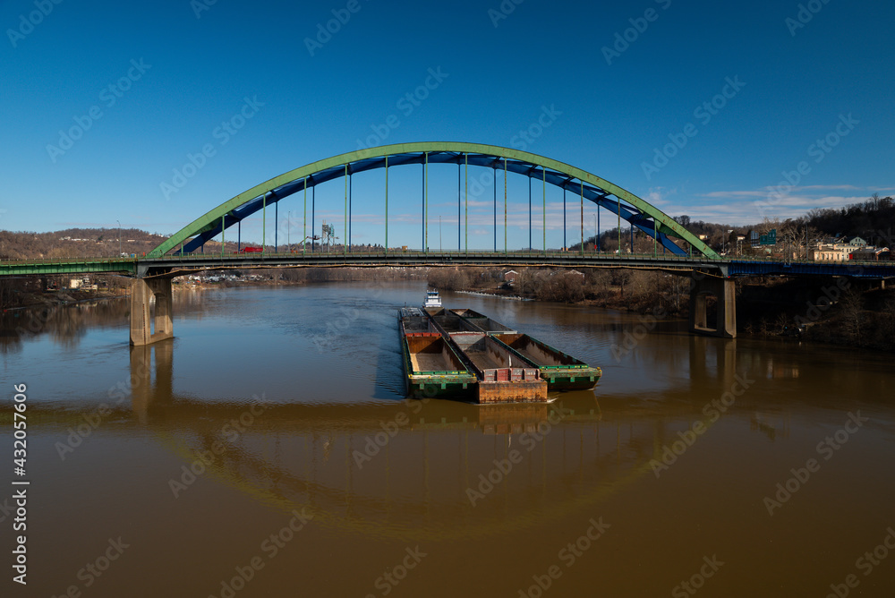 Fototapeta premium Fort Henry Arch Bridge with Barge Passing Underneath on Ohio River - Interstate 70 / US Routes 40 & 250 - Wheeling, West Virginia