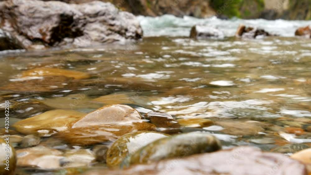 Ice melting cold crystal clear transparent shallow river water flowing over beautiful underwater stone, heavy stream in the background Ice melting cold crystal clear transparent shallow river water flowing over beautiful underwater stone, heavy stream in the background
