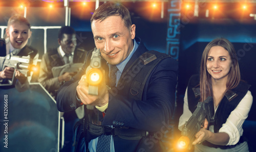 Man in business suit holding the his laser gun and playing laser tag with colleagues