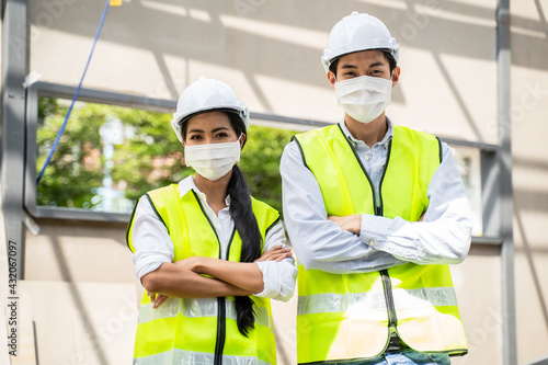 Asian male and female engineer wearing face mask, crossing arms.
