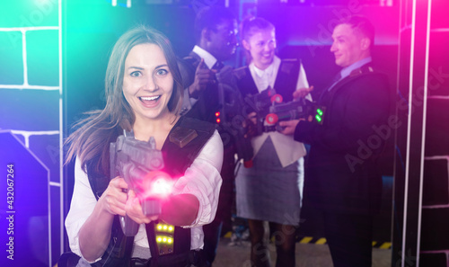 Emotional portrait of female playing laser tag with her co-workers on dark arena