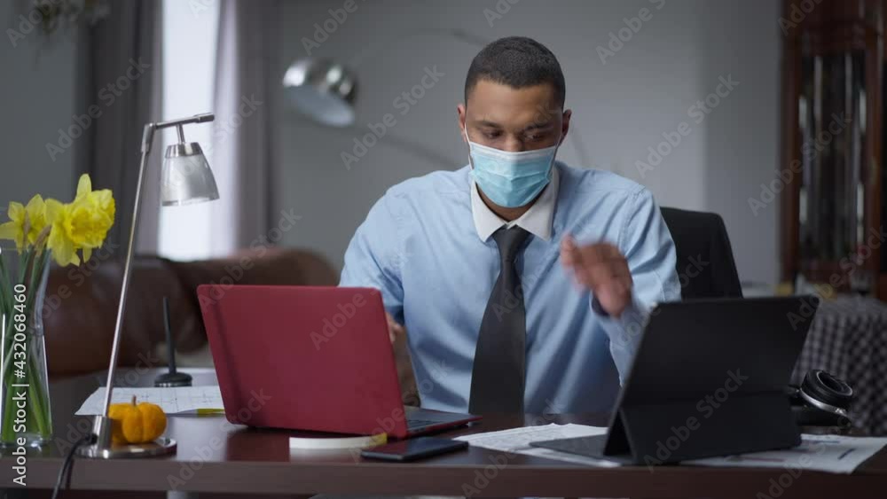 Portrait of overworking African American man in Covid face mask typing
