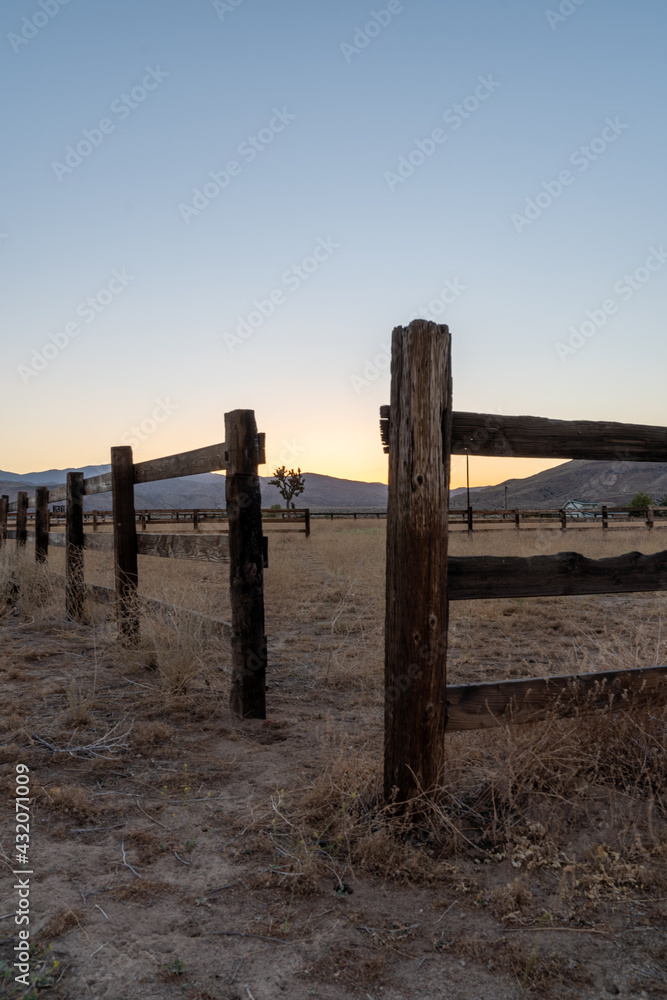 Sunset and an old wooden fence at California desert ranch in Pioneertown with a Joshua tree and mountains in the background.