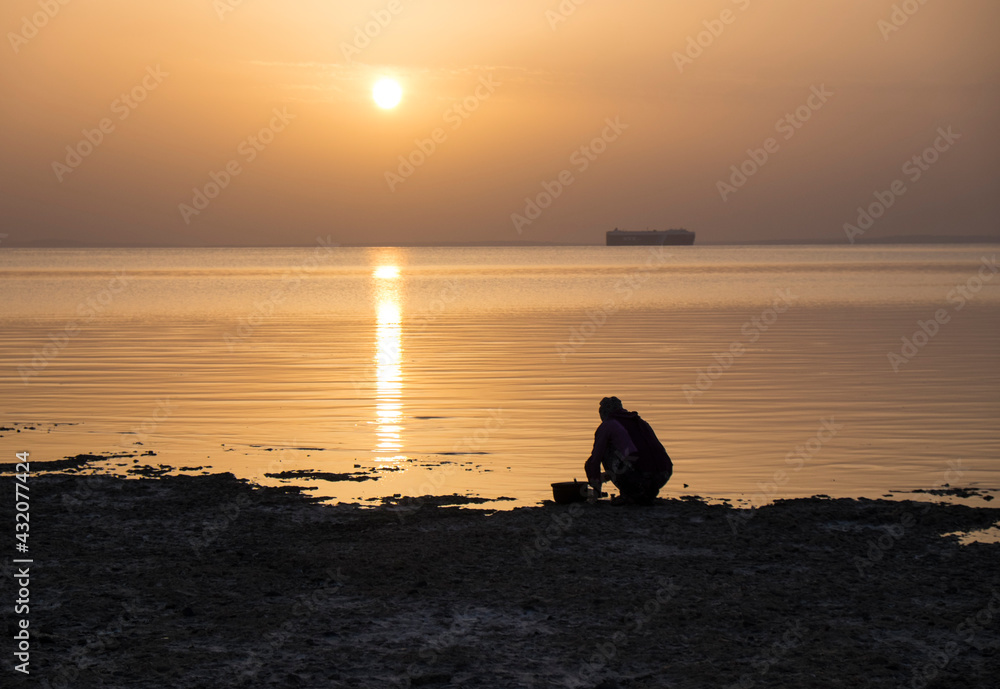 Woman washing dishes on the shore of the red sea at sunset