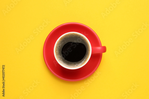 Aromatic coffee in red cup on yellow background, top view