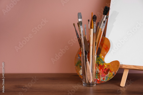 Easel with empty canvas and art supplies on wooden table. Space for text