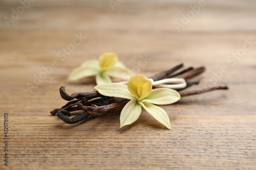 Aromatic vanilla sticks and flowers on wooden table, closeup