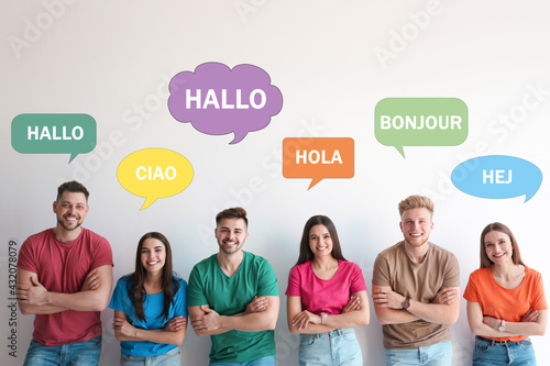 Happy people posing near light wall and illustration of speech bubbles with word Hello written in different languages photo