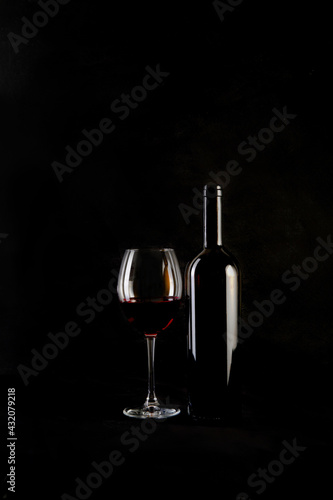 Red wine bottle with 2 glasses and bottle opener on black background.