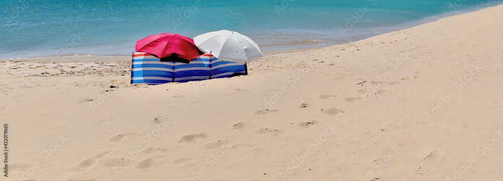 beach umbrellas windscreen sheltering people not visible alone on a beach with fine sand and turquoise sea
