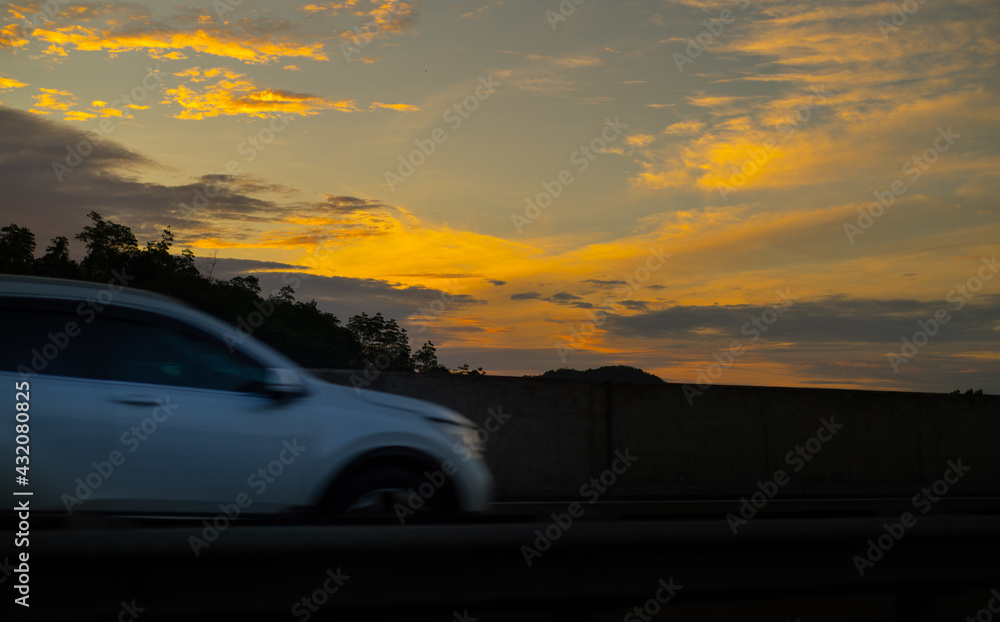 Fast moving car in expressway early in the morning against bright yellowish clouds.