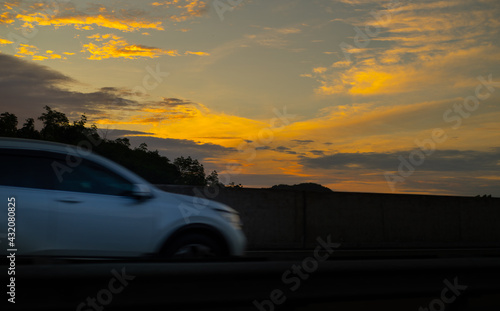 Fast moving car in expressway early in the morning against bright yellowish clouds. © nilanka
