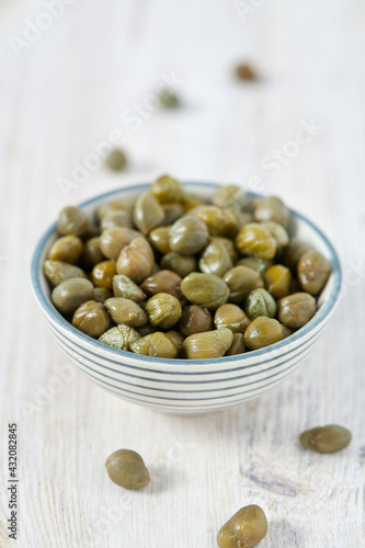 Pickled capers on white wooden surface. Gourmet food.