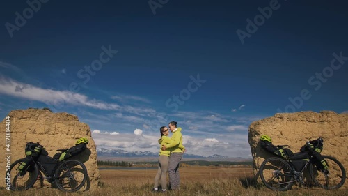 The man and woman travel on mixed terrain cycle touring with bikepacking. The two people journey with bicycle bags. Mountain snow capped, stone arch. photo