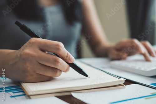 Close up hand of accountant taking note during calculate number with calculator.
