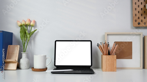 Mock up computer tablet, coffee cup and pencil holder on white table at home office.