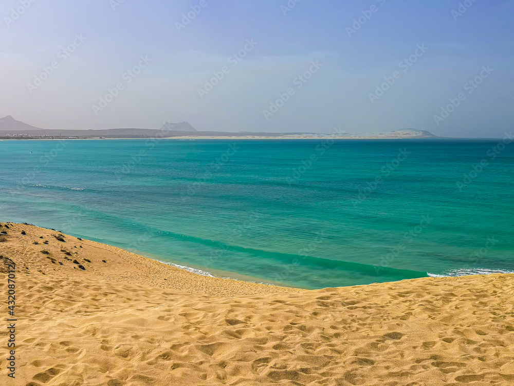 Atlantic Ocean view from a sand dune, Boa Vista Island, Cape Verde. Hot summer day on a tropical African bay. Selective focus on the footprint pattern, blurred background.