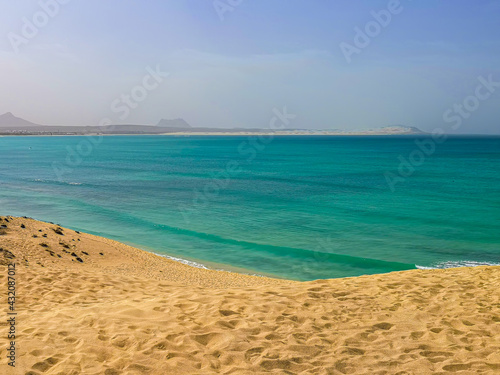 Fototapeta Naklejka Na Ścianę i Meble -  Atlantic Ocean view from a sand dune, Boa Vista Island, Cape Verde. Hot summer day on a tropical African bay. Selective focus on the footprint pattern, blurred background.