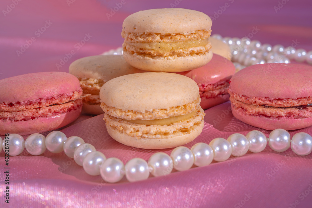 Pink and beige macarons on pink silk background with pearl necklace. French Pastel Macaroons. Selective focus