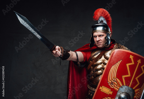 Obraz na plátně Angry roman soldier points sword against dark background