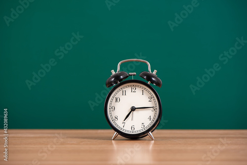Fototapeta Naklejka Na Ścianę i Meble -  Alarm clock over blackboard  on table background,back to school concept