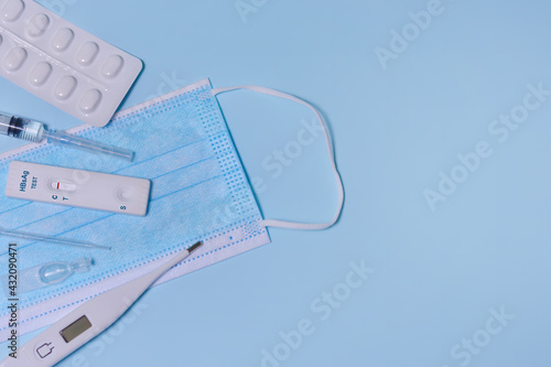 Rapid test cassette for Hepatitis B Virus Test (HBsAg),medical mask, syringe,thermometer,medicine on a blue background.Test shows a negative result. Copy space photo