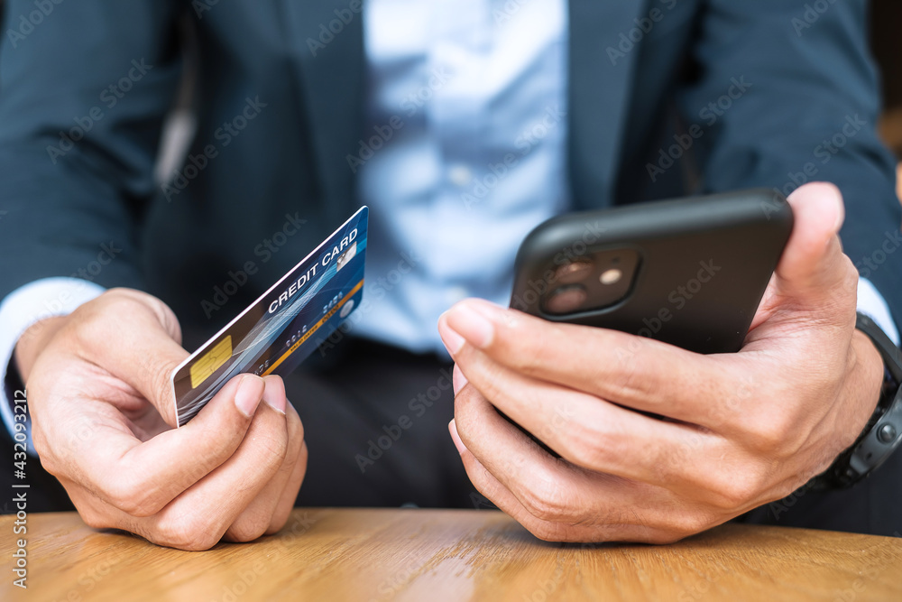 Businessman in suit holding credit card and using touchscreen smartphone for online shopping while making orders in the cafe or office .business, technology, ecommerce and online payment concept Businessman in suit holding credit card and using touchscreen smartphone for online shopping while making orders in the cafe or office .business, technology, ecommerce and online payment concept