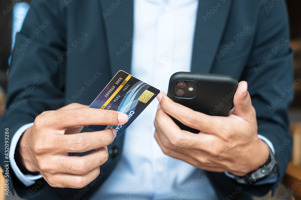 Businessman in suit holding credit card and using touchscreen smartphone for online shopping while making orders in the cafe or office .business, technology, ecommerce and online payment concept Businessman in suit holding credit card and using touchscreen smartphone for online shopping while making orders in the cafe or office .business, technology, ecommerce and online payment concept
