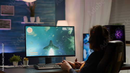 Back shot of pro gamer playing online space shooter game on powerful computer using wireless controller. Competitive cyber player woman performing video game tournament use professional joystick