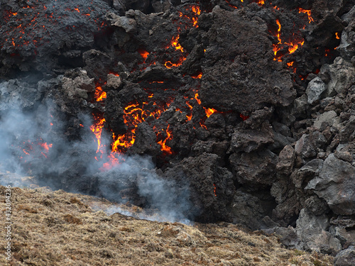 Close-up view of glowing lava rocks cooling down after volcanic eruption in Geldingadalir valley near Fagradalsfjall mountain, Grindavík, Reykjanes peninsula, southwest Iceland with burning grass. photo