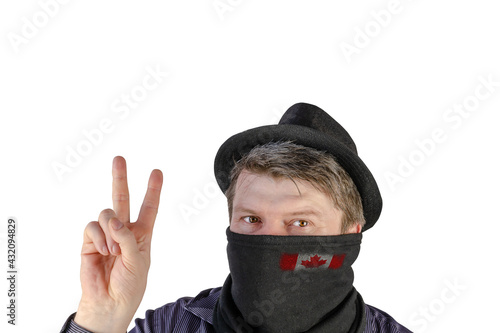 Adult man in a black hat with small fields and a scarf over his face shows a victory gesture.