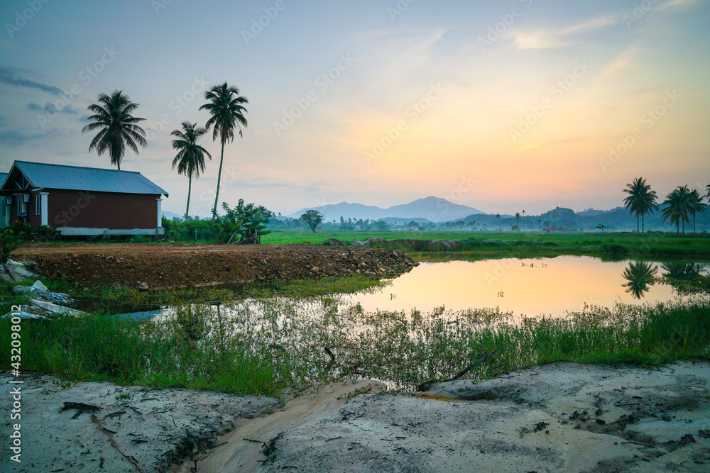 Landscape of countryside with a house, coconut trees, lake and hills at the horizon.