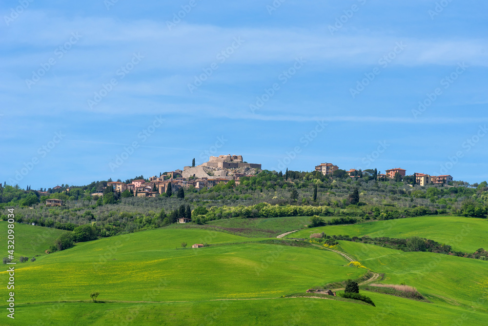 Panoramic landscape of the Italian Tuscan town with stone houses, a fortress on the mountain and green fields in spring.