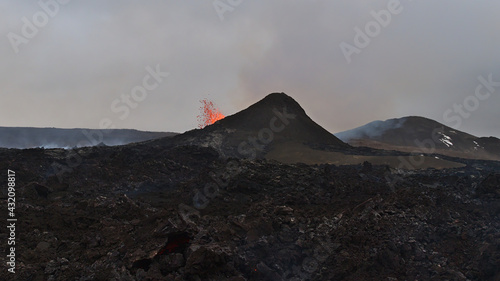 Stunning view of erupting volcano ejecting hot lava in Geldingadalir valley near Fagradalsfjall mountain, Grindavík, Reykjanes peninsula, southwest Iceland with black volcanic rocks in front.